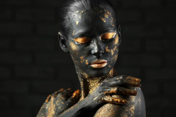 Beautiful woman with black and golden paint on her body against dark background — Stock Photo, Image