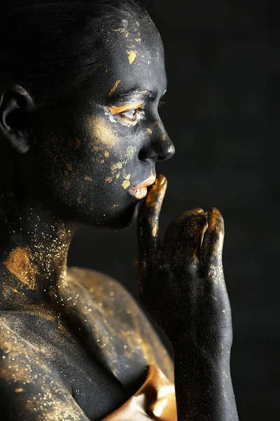 Beautiful woman with black and golden paint on her body against dark background — Stock Photo, Image