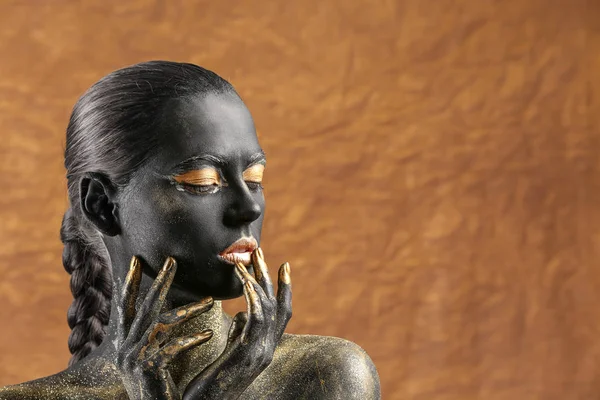 Beautiful woman with black and golden paint on her body against color background — Stock Photo, Image