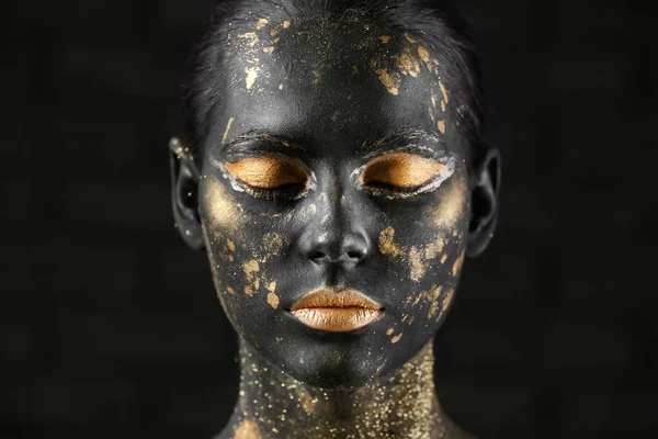 Beautiful woman with black and golden paint on her body against dark background — Stock Photo, Image