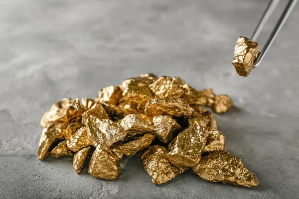 Taking of gold nugget with pincer from grey table — Stock Photo, Image