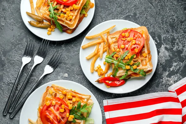 Delicious waffles with french fries and vegetables on plates
