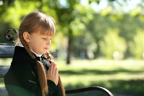 Little girl praying on bench outdoors — Stock Photo, Image