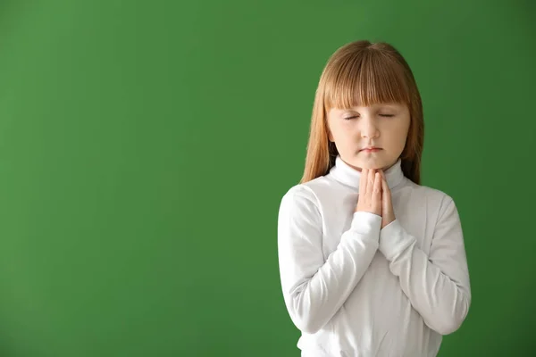 Маленька дівчинка молиться на кольоровому фоні — стокове фото