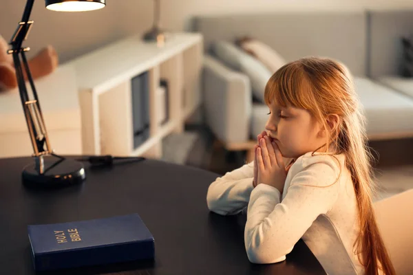 Little girl praying at dark table — Stock Photo, Image