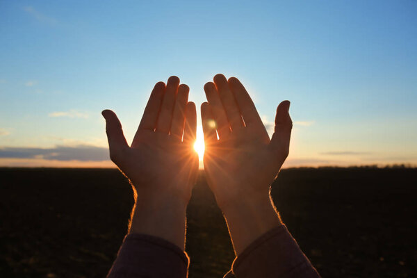 Руки религиозного человека молящегося на улице на закате
