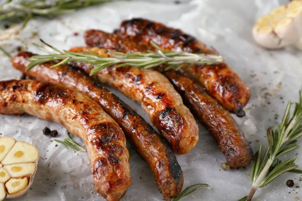 Leckere Grillwürste mit Rosmarin und Knoblauch auf Pergament — Stockfoto