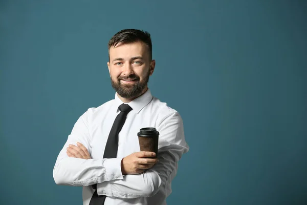 Handsome businessman with cup of coffee on color background — Stock Photo, Image