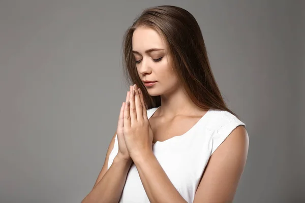 Piękna młoda kobieta, modląc się na szarym tle — Zdjęcie stockowe