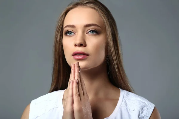 在灰色背景祈祷美丽的年轻妇女 — 图库照片