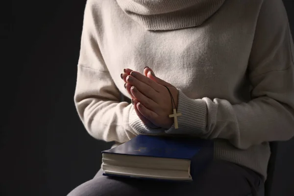 Young woman with Bible praying on dark background, closeup