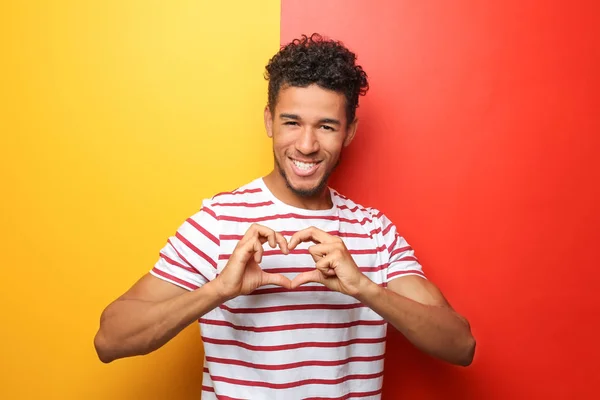 Handsome African-American man making heart with his hands on color background — Stock Photo, Image