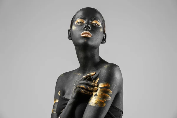 Schöne Frau mit schwarzer und goldener Farbe auf ihrem Körper vor hellem Hintergrund — Stockfoto
