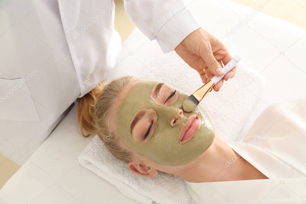 Cosmetologist applying mask with aloe vera extract onto face of young woman in beauty salon