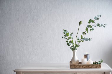 Beyaz masadaki vazoda yeşil yapraklarla yanan güzel mumlar.