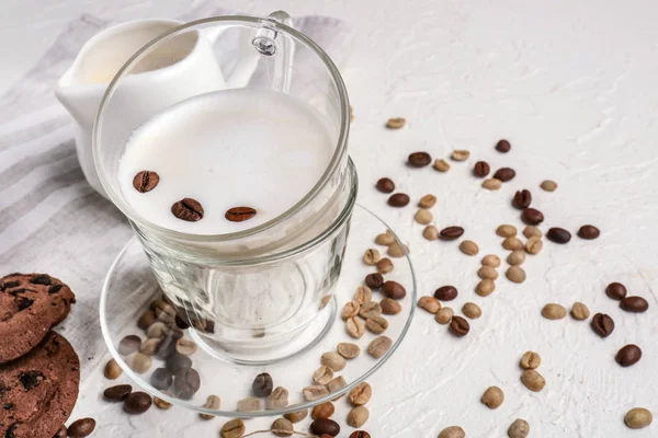 Glass cup of tasty milk with coffee beans on white table — Stock Photo, Image