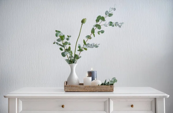 Belles bougies allumées avec des feuilles vertes dans un vase sur une table blanche — Photo