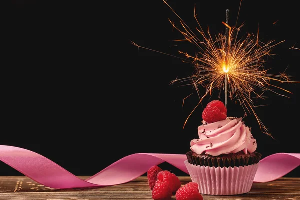 Delicious birthday cupcake with firework candle on table against dark background — Stock Photo, Image