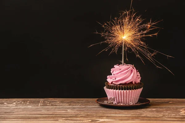 Bolo de aniversário delicioso com vela de fogo de artifício na mesa contra fundo escuro — Fotografia de Stock