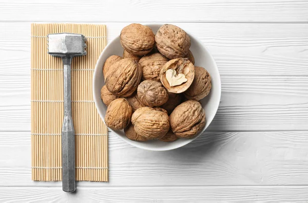 Тарелка с вкусными грецкими орехами и молотком на белом деревянном столе — стоковое фото