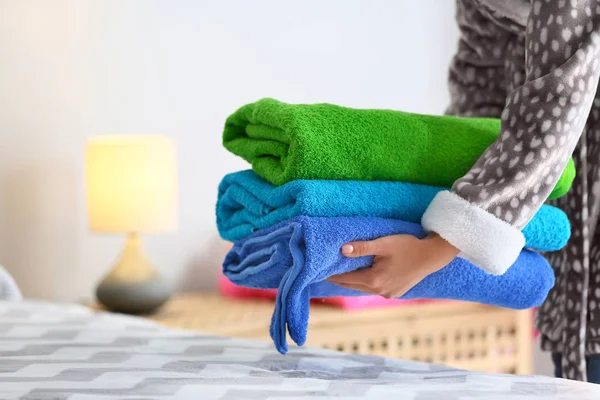 Woman putting stack of clean towels on bed — Stock Photo, Image