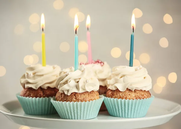 Läckra birthday cupcakes med brinnande ljus på tallrik — Stockfoto