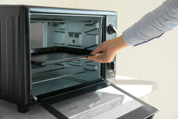 Woman putting baking tray into electric oven — Stock Photo, Image