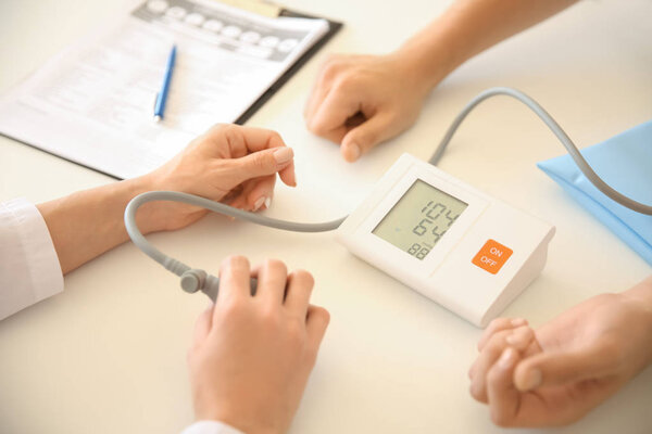 Female doctor measuring blood pressure of male patient in hospital