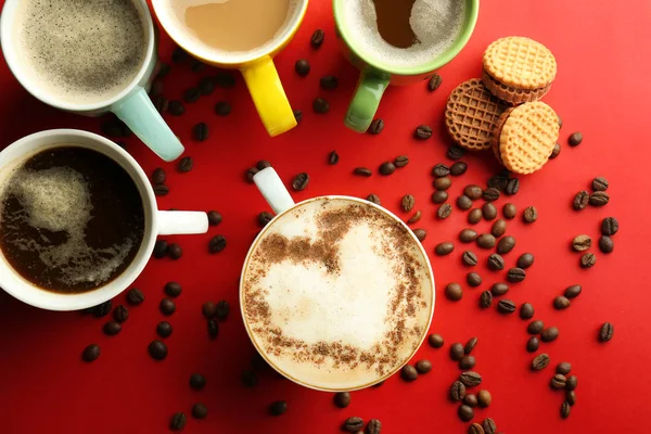 Veel kopjes met smakelijke aromatische koffie en koekjes op kleur achtergrond, plat leggen — Stockfoto