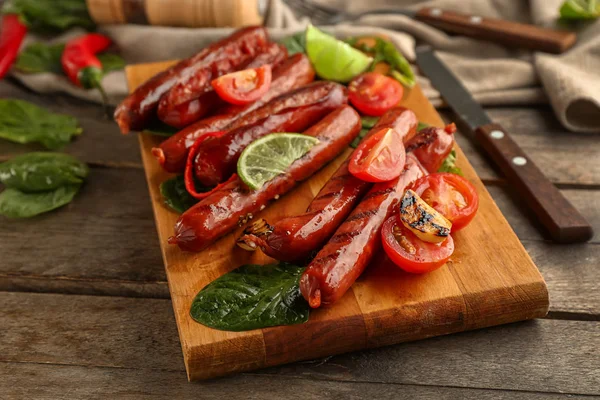 Wooden board with delicious grilled sausages and vegetables on table — Stock Photo, Image