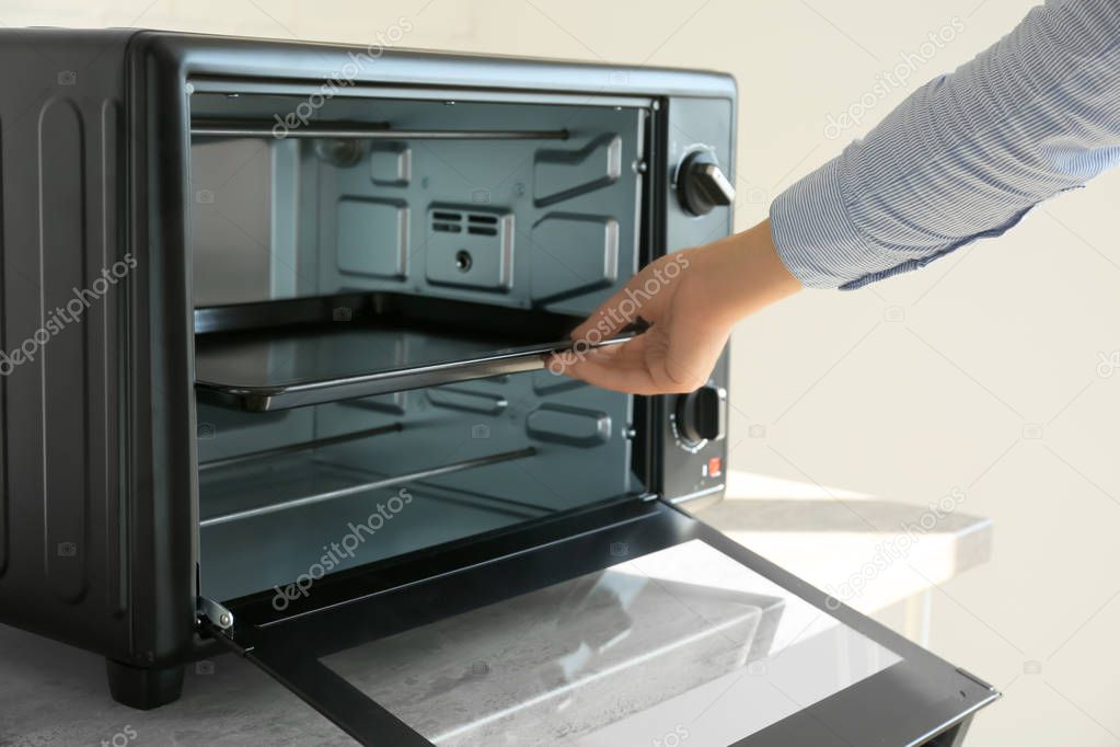Woman putting baking tray into electric oven