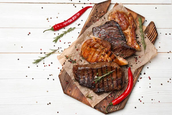 Wooden board with different tasty cooked meat and spices on white table — Stock Photo, Image