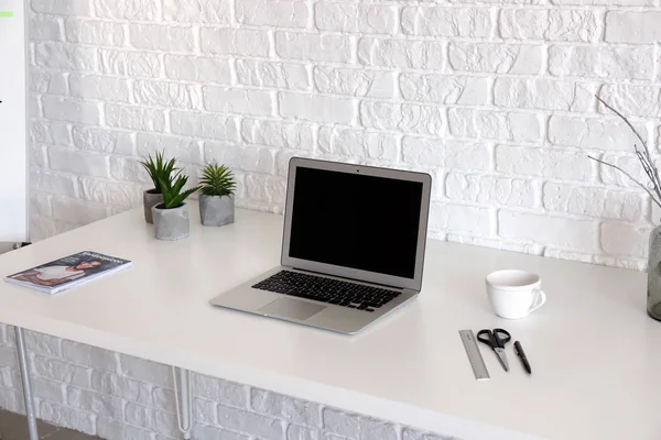 Portátil moderno en la mesa de luz cerca de la pared de ladrillo blanco — Foto de Stock