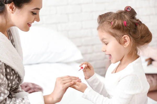 Cute daughter with mother curling hair and making manicure at home