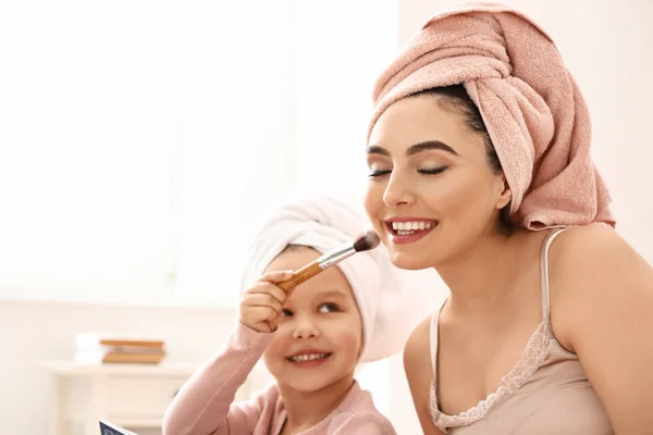 Filhinha aplicando cosméticos no rosto de sua mãe em casa — Fotografia de Stock