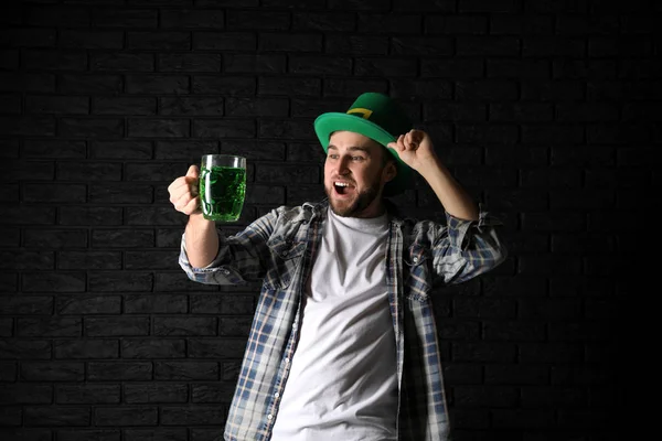 Giovanotto emotivo in cappello verde e con boccale di birra su sfondo scuro. Festa di San Patrizio — Foto Stock