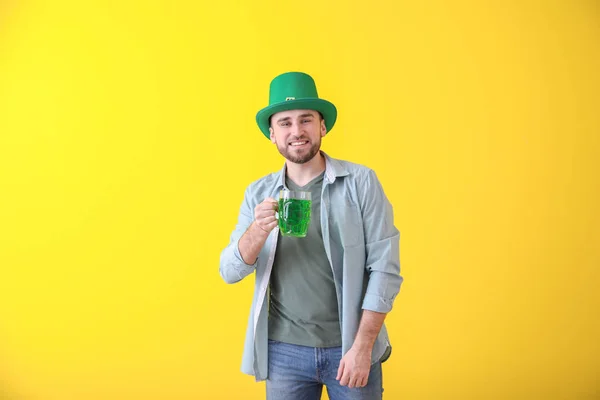 Jovem bonito em chapéu verde e com caneca de cerveja no fundo de cor. Celebração do Dia de São Patrício — Fotografia de Stock