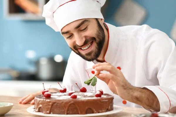 Мужской кондитер украшает вкусный шоколадный торт на кухне — стоковое фото