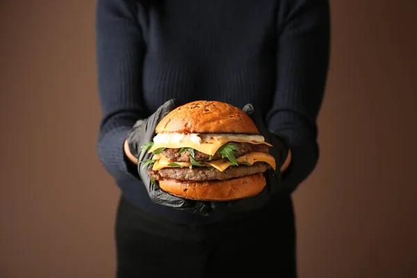 Mujer sosteniendo sabrosa hamburguesa sobre fondo de color — Foto de Stock