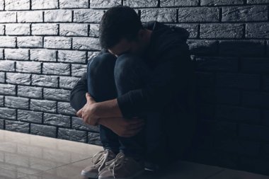 Depresif adam otururken karanlık tuğla duvarının yakınında intihar hakkında düşünme