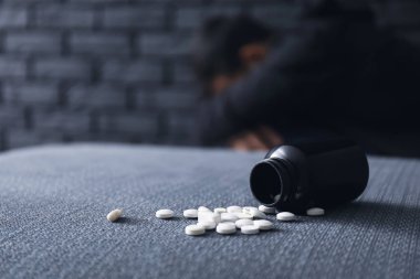Overturned bottle with pills and depressed man on background. Suicide awareness concept clipart