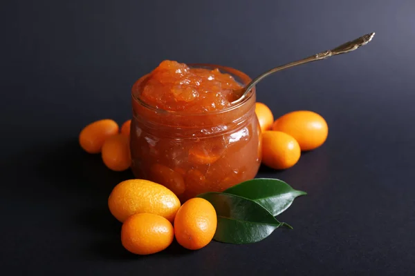 Jar with delicious kumquat jam on dark background — Stock Photo, Image