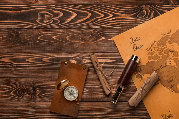 Spyglass, pergaminos, brújula, cuaderno y mapa del mundo sobre fondo de madera. Concepto de viaje — Foto de Stock