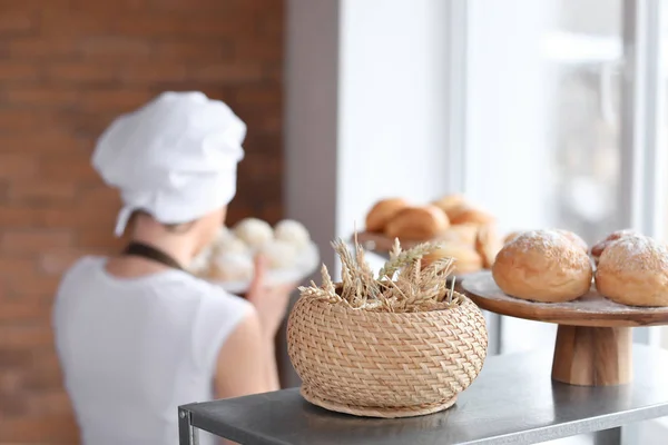Wicker basket with wheat ears and fresh buns on shelf in bakery shop — Stock Photo, Image