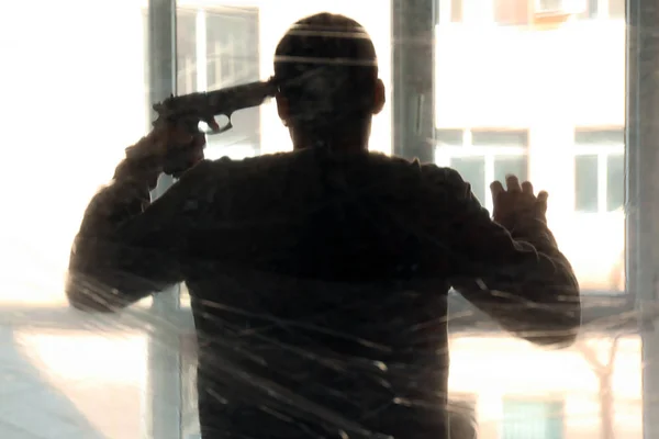 Silueta de hombre joven con arma de fuego va a suicidarse cerca de la ventana — Foto de Stock