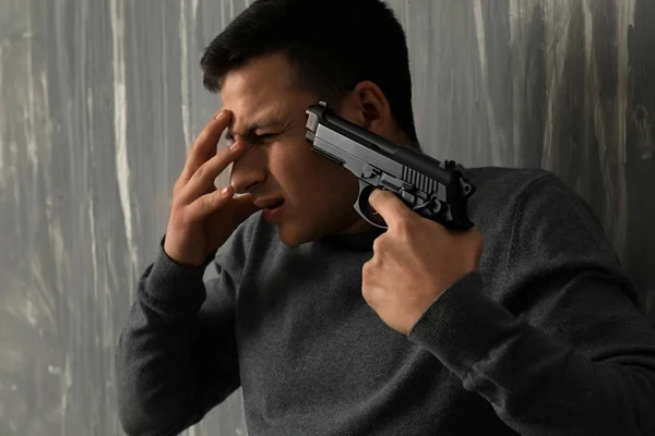 Depressed man with gun going to commit suicide against grunge background — Stock Photo, Image