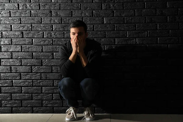 Депрессивный человек думает о самоубийстве, сидя возле темной кирпичной стены — стоковое фото