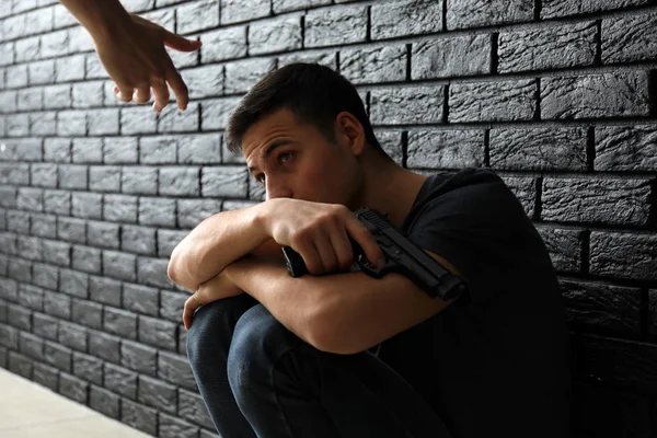 Mujer dando la mano a un hombre deprimido con un arma cerca de la pared oscura. Concepto de prevención del suicidio — Foto de Stock