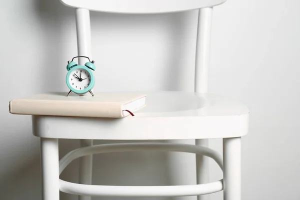 Relógio despertador e cadeira livro contra fundo branco — Fotografia de Stock