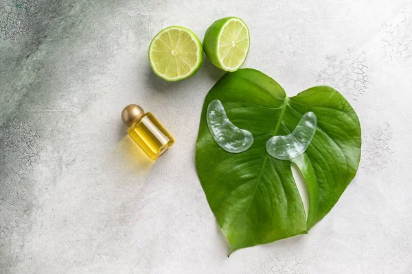 Under-eye patches with essential oil and lime on light background